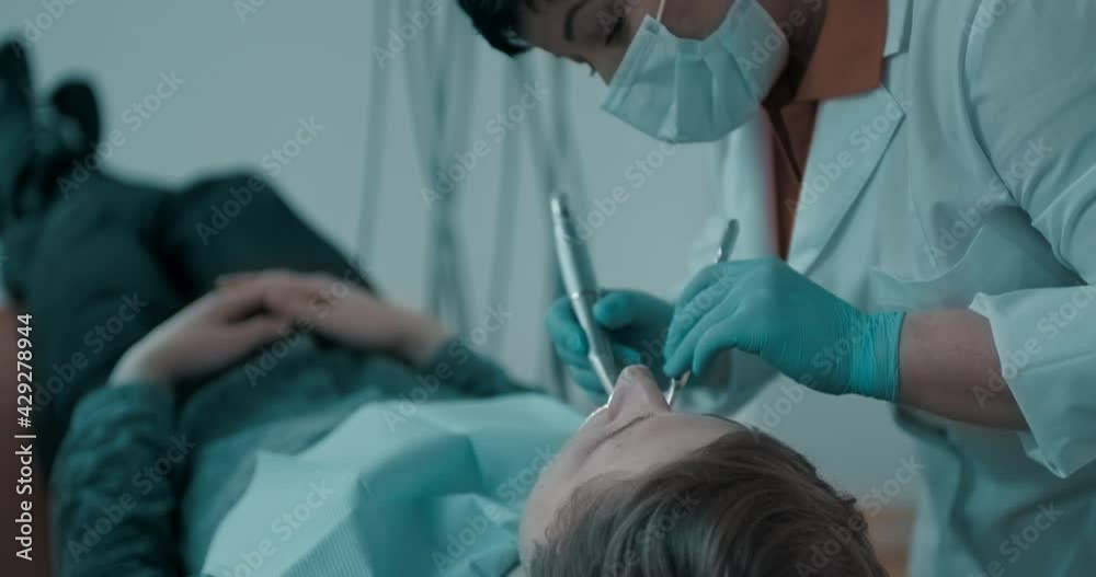 The female dentist is taking from the dental holder the dental drill for use in the dental treatment of a male patient. The female dentist is taking from the dental holder the dental drill for use in the dental treatment of a male patient.