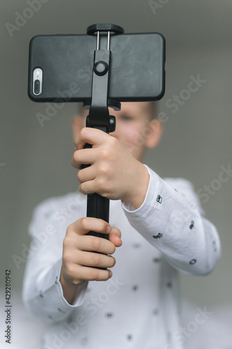 A seven-year-old boy, in light-colored clothes, holds a phone in his hands, takes pictures, conducts video chat with friends, communicates with people in quarantine. Modern technologies