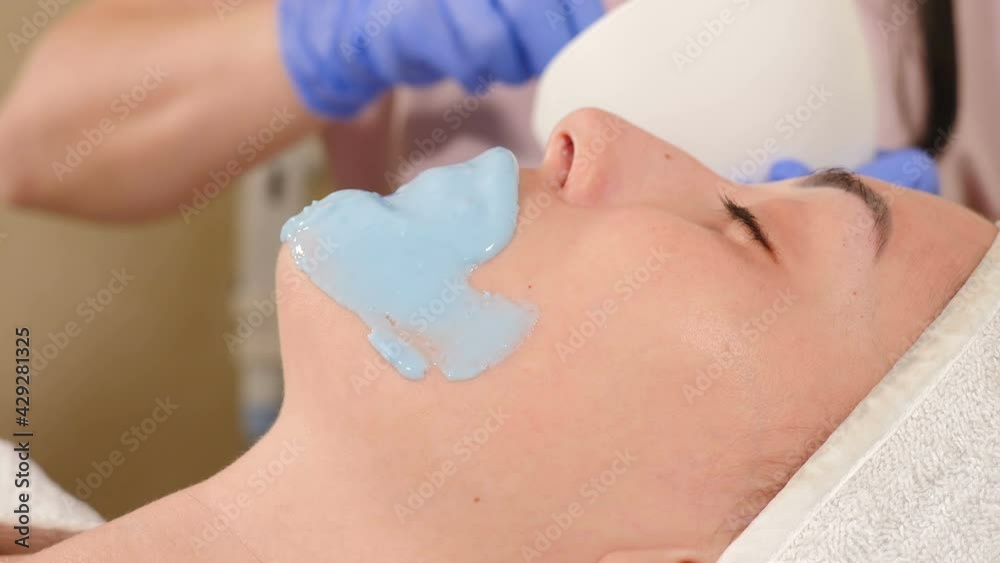 Cosmetologist applies alginate mask with spatula on female. Facial skin and anti-aging treatment. Cosmetology and professional facial skin care concept. young woman getting alginate mask on face, 4 k Cosmetologist applies alginate mask with spatula on female. Facial skin and anti-aging treatment. Cosmetology and professional facial skin care concept. young woman getting alginate mask on face, 4 k