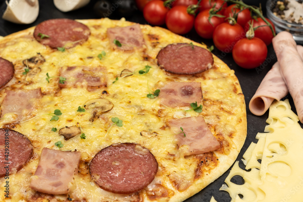 Pizza with ham, salami and mushrooms on a black background close-up with ingredients. Pizza with ham, salami and mushrooms on a black background close-up with ingredients.