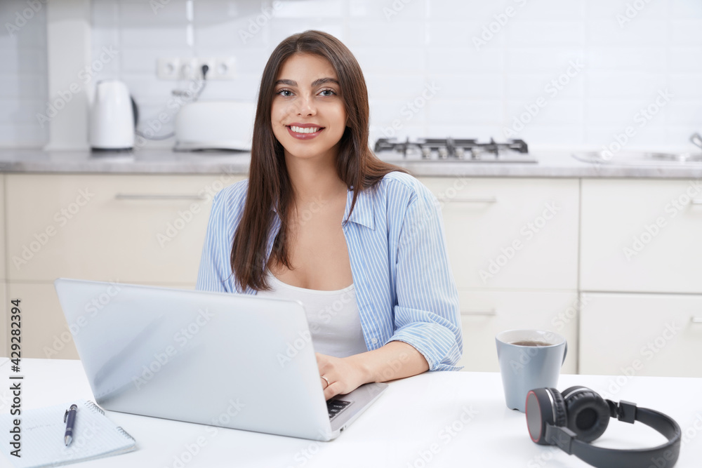 Close up of young smiling beautiful woman using laptop for working or studying at home. Concept of process working or studying in kitchen.