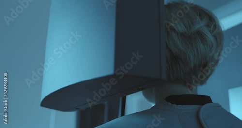 Close-up back view a woman patient who is standing in the 3D dental tomography scan which is rotating around of her head and providing a full mouth x-ray.