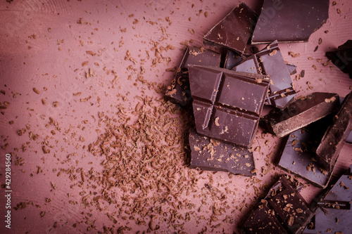 Flat lay of pieces of chocolate bar with chocolate chips on brown background. Broken chocolate pieces.