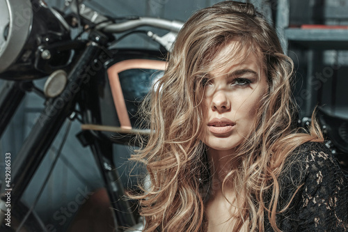 Sensual woman. Sexy girl face sitting near motorcycle on garage background. Motorcycling, hobby and lifestyle.