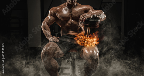 Muscular man sits on a bench with dumbbells burning. Bodybuilding and powerlifting concept.