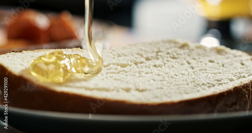 A trickle of honey flows down onto a piece of bread. Honey, breakfast