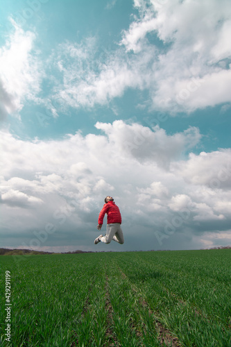 Man jumping on a green meadow with a beautiful cloudy sky