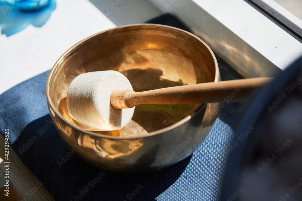 The mallet from a singing bowl lies in the singing bowl. It is on blue background and stands on a window sill. Daylight. Light supervision. The mallet from a singing bowl lies in the singing bowl. It is on blue background and stands on a window sill. Daylight. Light supervision.