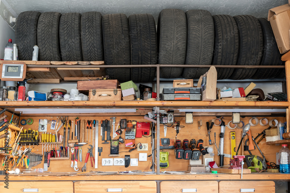 Home suburban garage interior big wooden workbench with lot of power  mechanic tools at background. Spare season wheels storage shelf rack  ceiling warehouse. DIY, self service and repair Stock-Foto | Adobe Stock