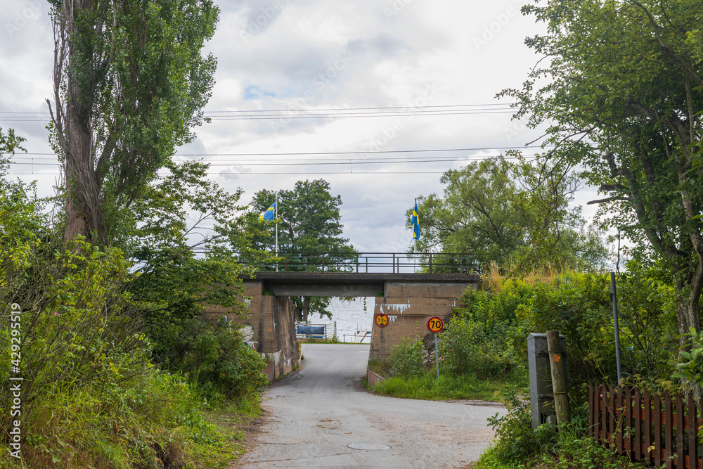 Beautiful landscape view. Small road passing under bridge. Green trees on cloudy sky background. Sweden. Beautiful landscape view. Small road passing under bridge. Green trees on cloudy sky background. Sweden.