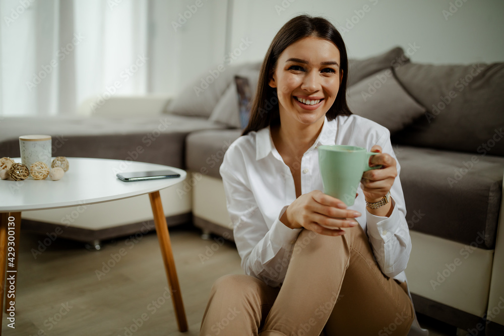 Young pretty lady sitting on the floor and looking at camera while drinking coffee. Young pretty lady sitting on the floor and looking at camera while drinking coffee.