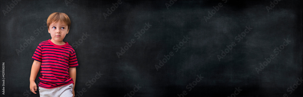 Little boy leaning against a blank blackboard, ready to be written, drawn or used as a mockup. Kid with mischief face. Little boy leaning against a blank blackboard, ready to be written, drawn or used as a mockup. Kid with mischief face.