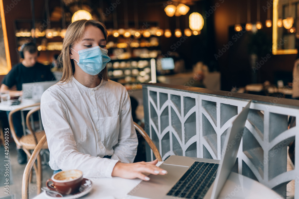 Pretty woman wearing medical face mask, using laptop to work.