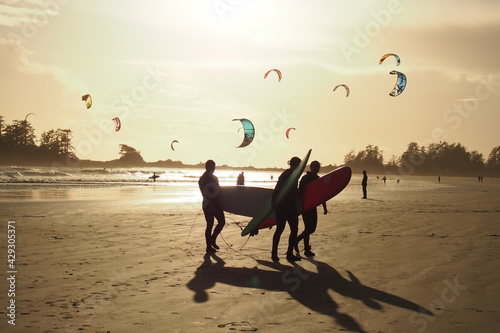 Group of Surfers enjoy themselves in foreground of windsurfing enthusiasts at a beach at golden hour