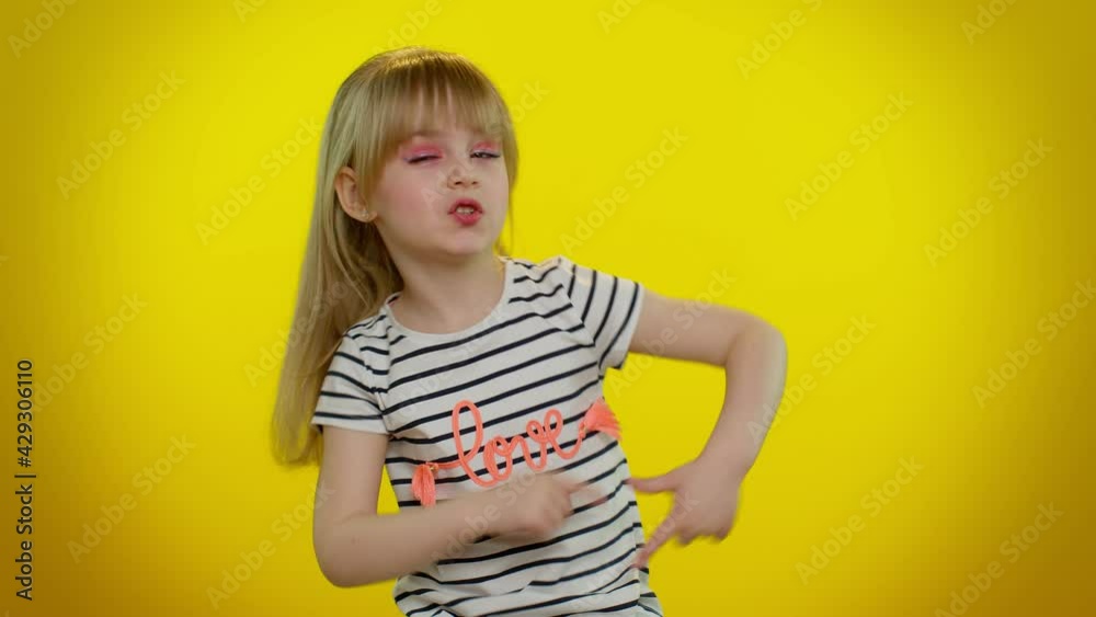 Little blonde teen kid child girl in t-shirt pointing around with finger gun gesture, looking confident, making choice, shooting killing with hand pistol right on target on yellow studio background Little blonde teen kid child girl in t-shirt pointing around with finger gun gesture, looking confident, making choice, shooting killing with hand pistol right on target on yellow studio background