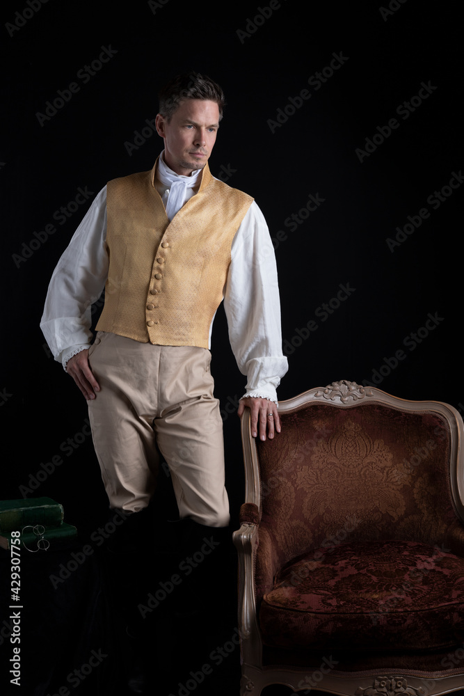 A handsome Regency gentleman standing beside a red velvet chair in a darkened room A handsome Regency gentleman standing beside a red velvet chair in a darkened room