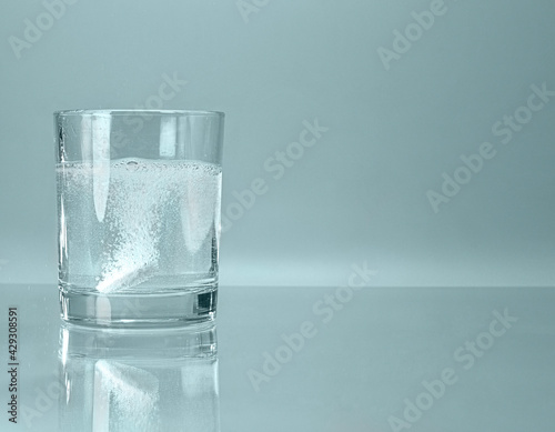 A glass with a effervescent soluble tablet bubbling on the bottom of turquoise blue water.