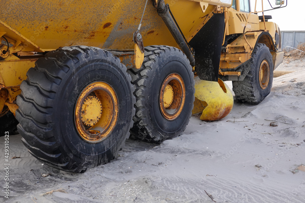 Large heavy duty tires on a large yellow construction vehicle on a sandy beach Large heavy duty tires on a large yellow construction vehicle on a sandy beach