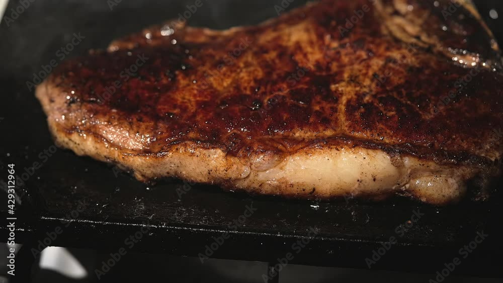 This slow motion video shows a close up view of a juicy steak sizzling and being flipped over the edge of a flat top cooking area. This slow motion video shows a close up view of a juicy steak sizzling and being flipped over the edge of a flat top cooking area.