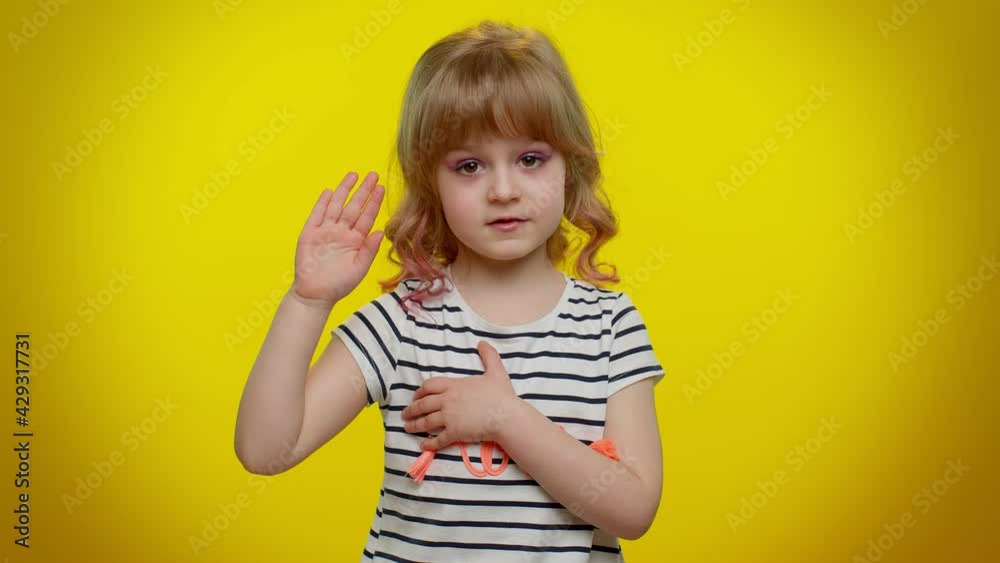 I swear to be honest. Responsible sincere little kid child in shirt raising hand to take oath, promising to be honest and to tell truth, keeping hand on chest on yellow wall. Children girl emotions I swear to be honest. Responsible sincere little kid child in shirt raising hand to take oath, promising to be honest and to tell truth, keeping hand on chest on yellow wall. Children girl emotions