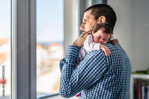 Φωτογραφία Side view of father holding his newborn baby over the shoulder while standing by