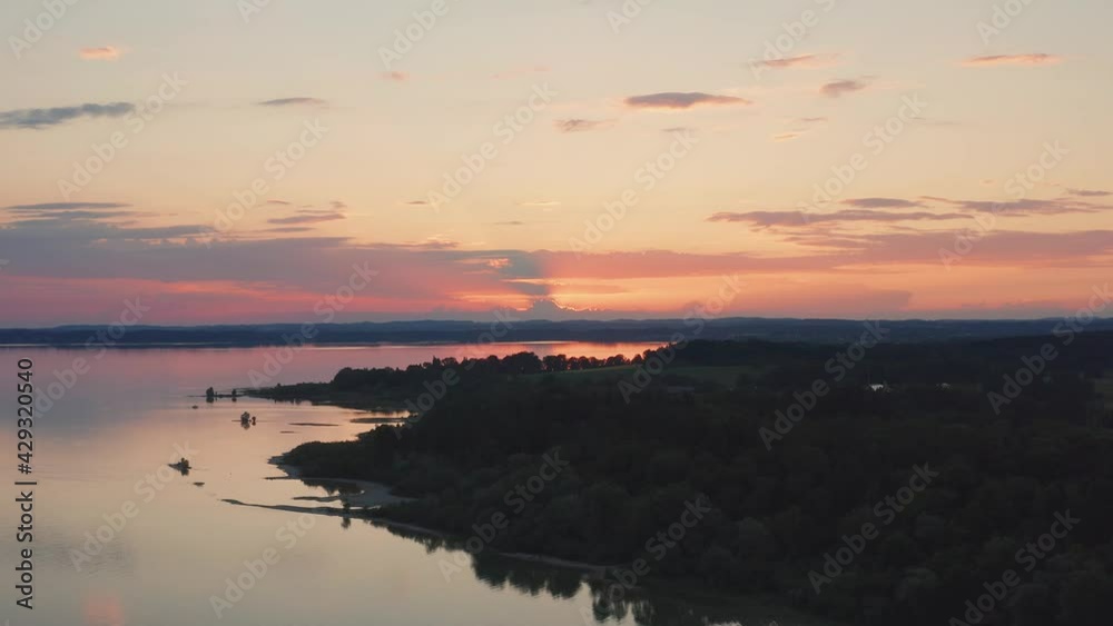 Lake Chiemsee in Bavaria with the Alp mountains during sunset from above, coast near village Chieming, during summer, flying upwards
