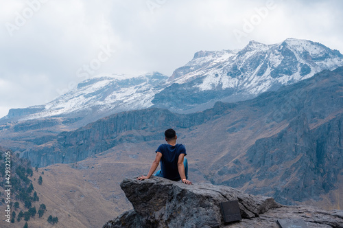 Back view of a man admiring the beauty of Iztaccihuatl volcanic mountain sitting alone on a stone photo