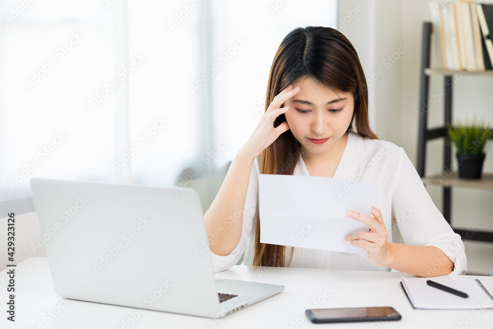 Young asian business woman hand touching head looking at paper work or bills she's feeling depressed stress headache be tired from working with laptop a long time she symptom office syndrome. Young asian business woman hand touching head looking at paper work or bills she's feeling depressed stress headache be tired from working with laptop a long time she symptom office syndrome.
