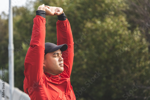 Young asian man wearing sportswear running outdoor. Portraits of Indian man stretching arm before running on the road. Training athlete work out at outdoor concept.