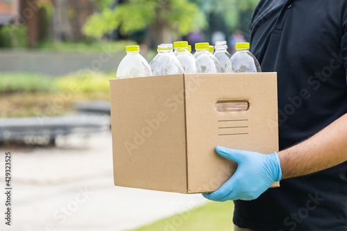 A young man wearing rubber gloves arranged plastic bottles into a carton. He assumes plastic bottles will sort of trash before throwing them into the bin.