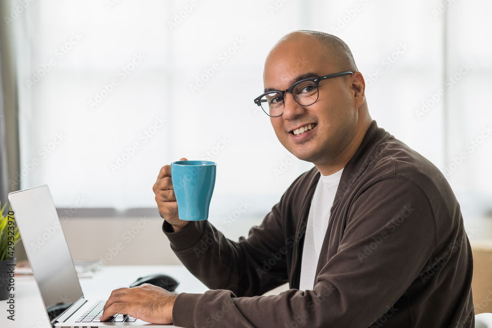 Indian man using laptop sitting in living room texting on laptop sending message or chatting with online social media.