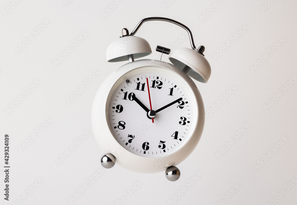 Small white alarm clock, black numbers, set the time for 10.10 o'clock, placed on a white table. Small white alarm clock, black numbers, set the time for 10.10 o'clock, placed on a white table.