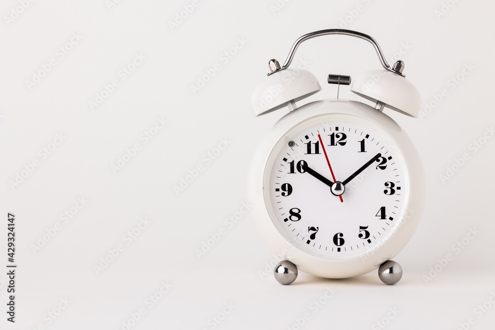 Small white alarm clock, black numbers, set the time for 10.10 o'clock, placed on a white table. Small white alarm clock, black numbers, set the time for 10.10 o'clock, placed on a white table.