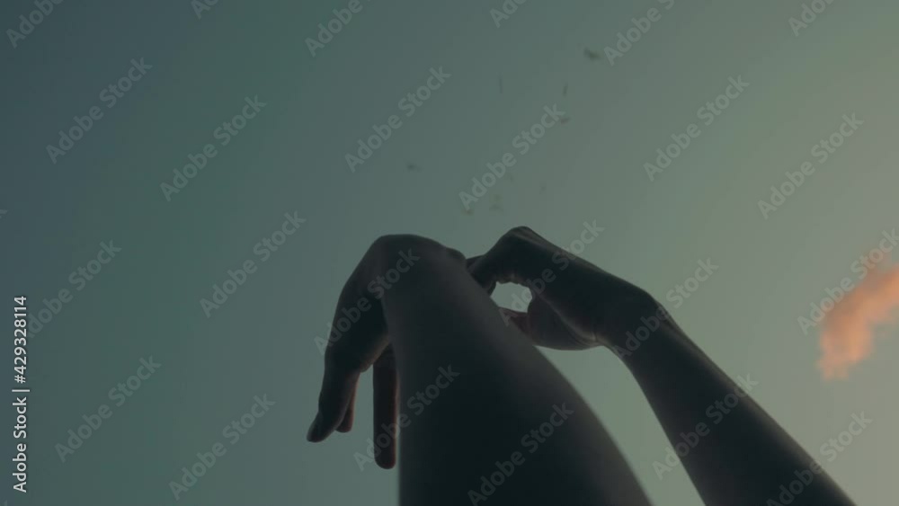 Slow-motion low angle of hands raised to sky moving like dancing while leaves fall from above