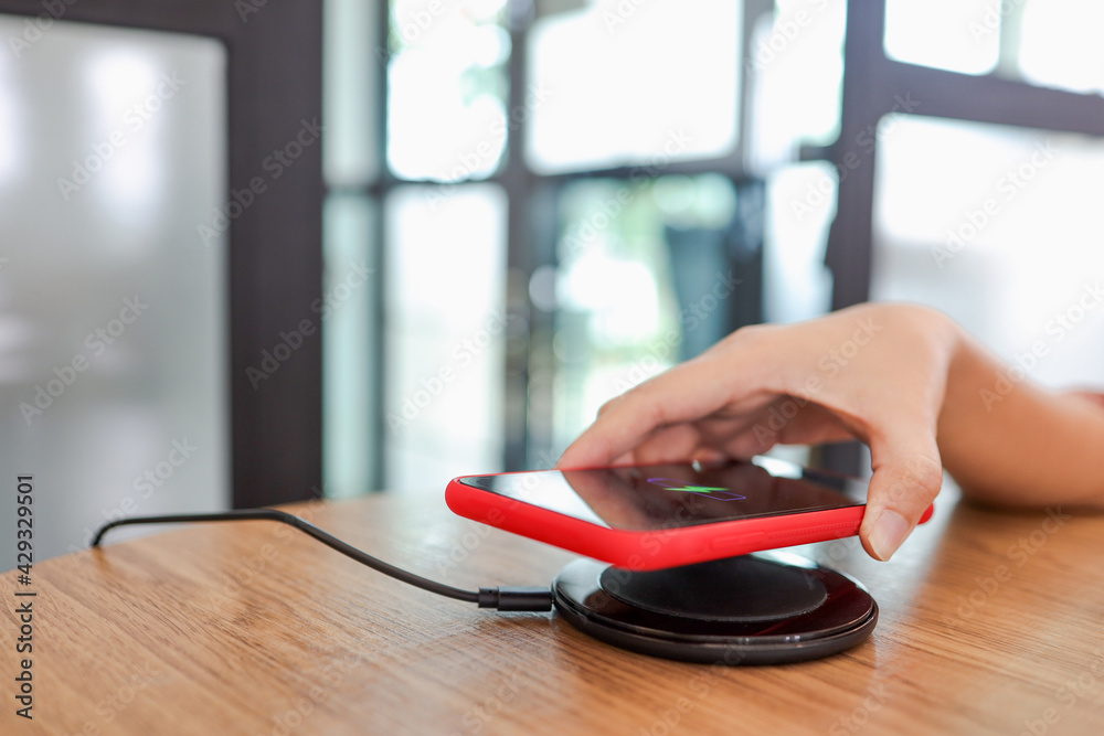 Fototapeta premium Charging mobile phone battery with wireless device in the table. Smartphone charging on a charging pad. Mobile phone near wireless charger.