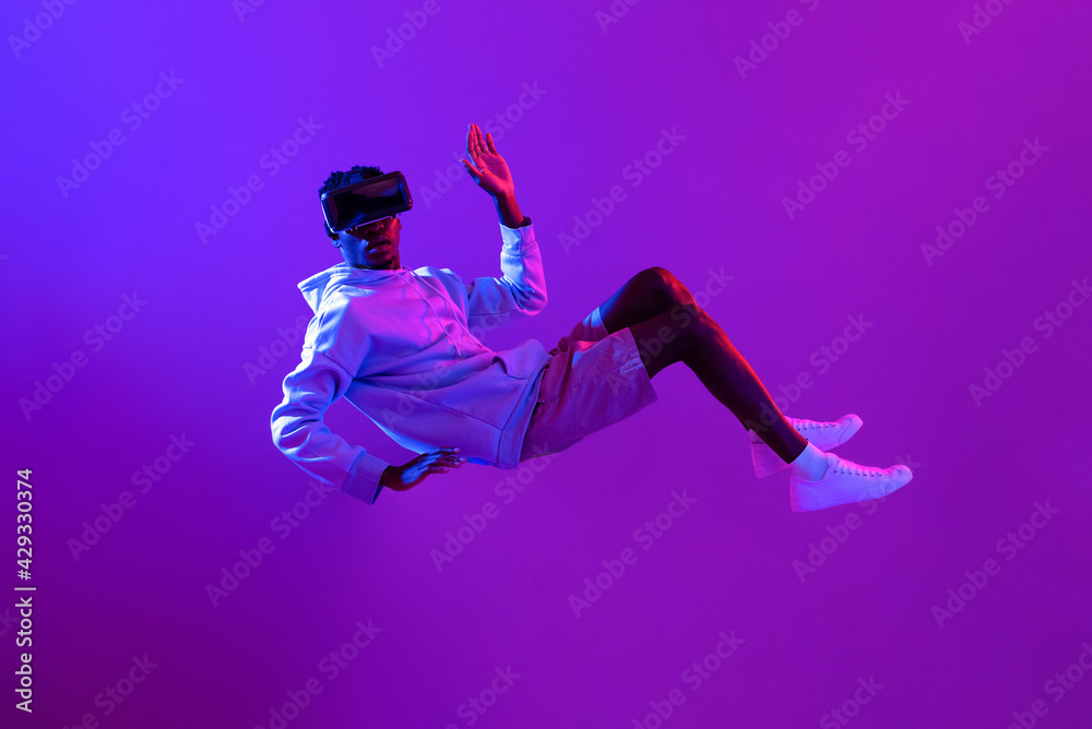 Amazed young African man wearing VR glass headset levitating in the air on  futuristic purple cyberpunk neon light background foto de Stock | Adobe  Stock