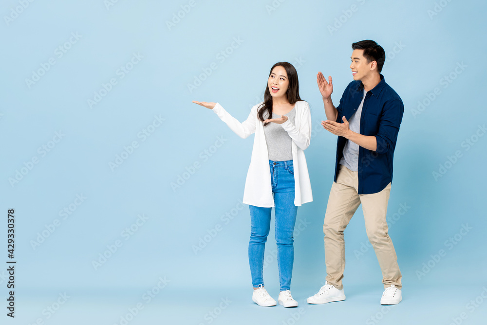 Smiling excited Asian couple tourists pointing hands to empty space aside on isolated light blue background Smiling excited Asian couple tourists pointing hands to empty space aside on isolated light blue background
