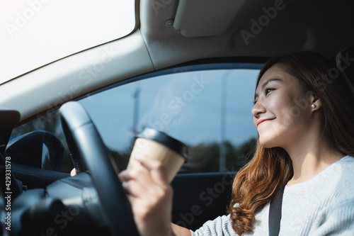A young asian woman holding and drinking coffee while driving a car © Farknot Architect