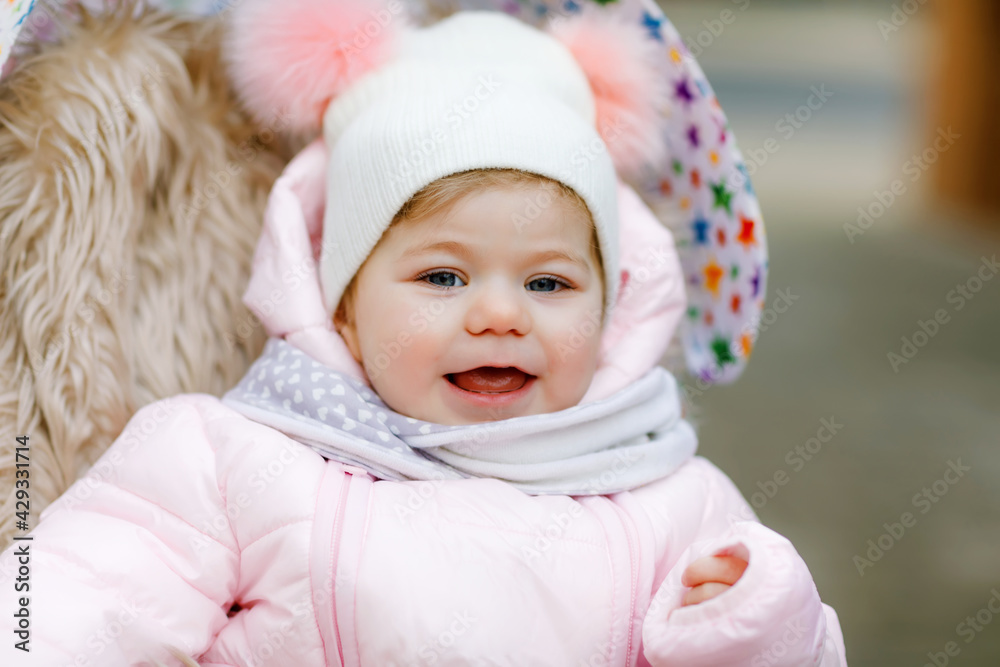 Cute little beautiful baby girl sitting in the pram or stroller on cold autumn, winter or spring day. Happy smiling child in warm clothes, fashion stylish baby coat and hat. Snow falling down Cute little beautiful baby girl sitting in the pram or stroller on cold autumn, winter or spring day. Happy smiling child in warm clothes, fashion stylish baby coat and hat. Snow falling down