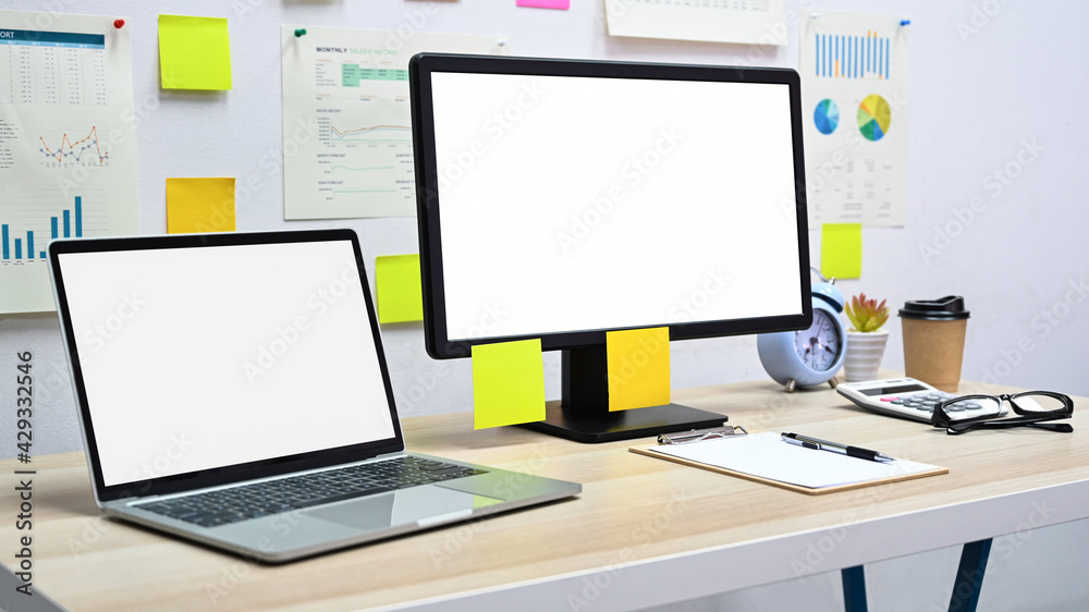 Blank screen mockup computer and laptop with office equipment on the desk in the office. Blank screen mockup computer and laptop with office equipment on the desk in the office.