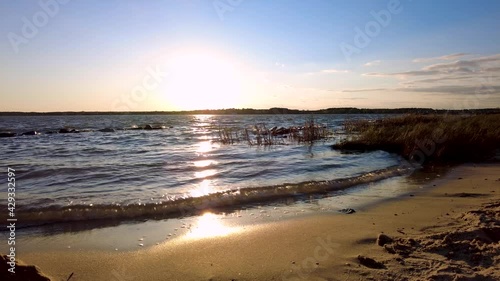 View of the sunset across Chesapeake bay as seen from the town of Oxford on the coast of Tred Avon River leading to the bay. There are sand grasses on the beach. Sunlight reflects from water.