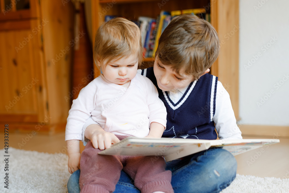 School kid boy reading book for little toddler baby girl, Two siblings sitting together and read books. Beautiful lovely family in love, cute baby and child having fun at home, indoors. School kid boy reading book for little toddler baby girl, Two siblings sitting together and read books. Beautiful lovely family in love, cute baby and child having fun at home, indoors.