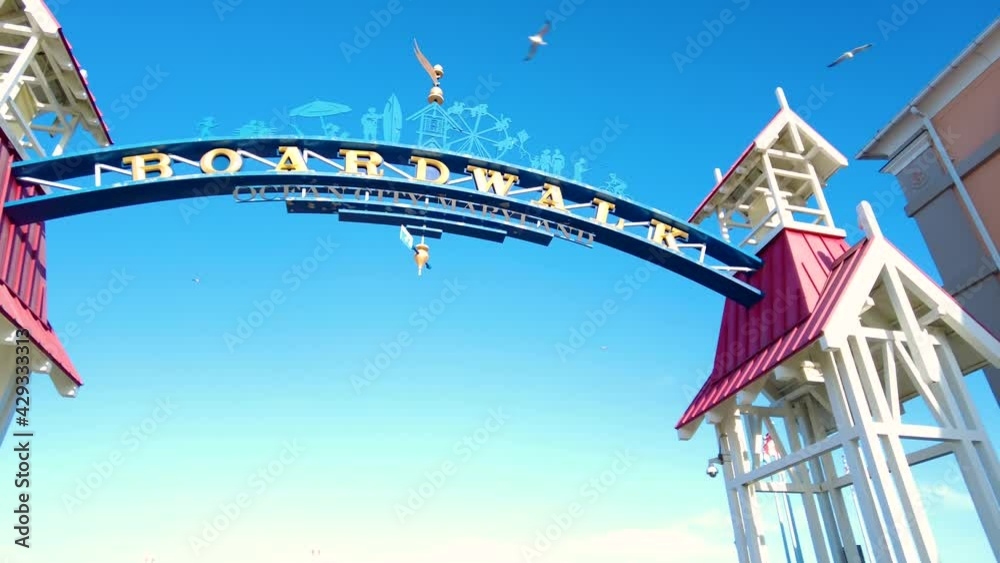   footage of the entrance of famous board walk by the Ocean City, Maryland beach where people are walking on a sunny afternoon. A popular tourist spot on east coast of USA