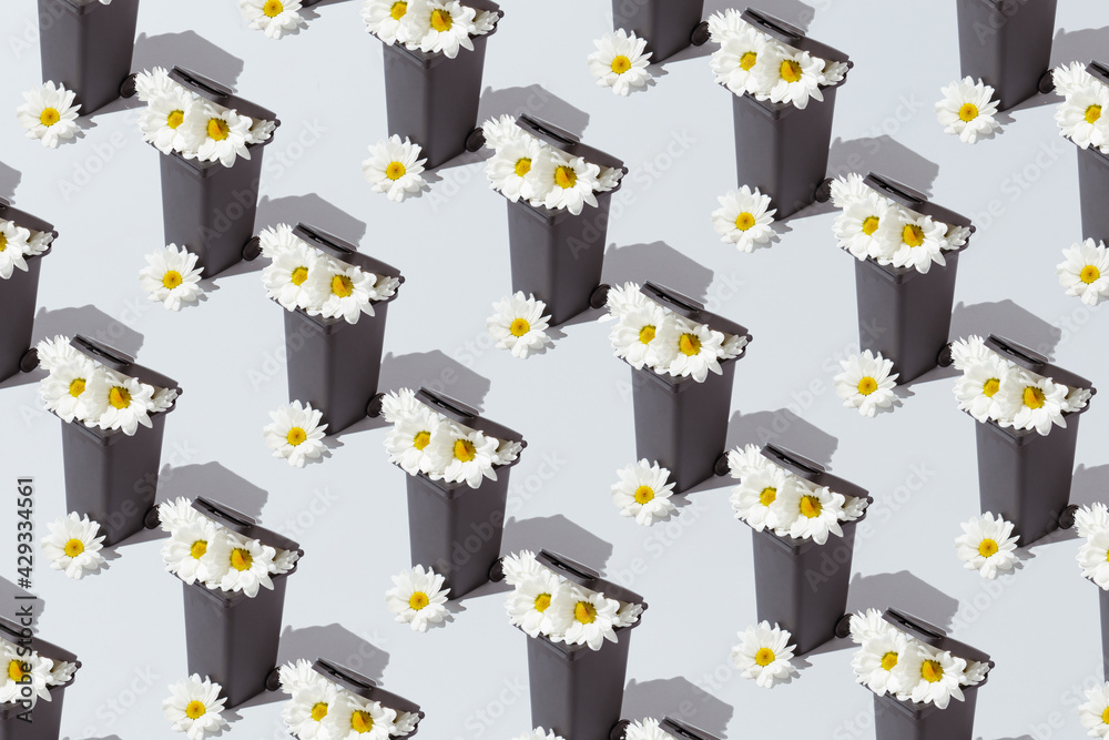 A creative nature pattern with white flowers growing from a trash can against a gray background. Minimal spring and nature concept A creative nature pattern with white flowers growing from a trash can against a gray background. Minimal spring and nature concept