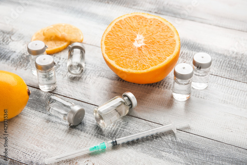 Quadro su tela Ampules with vitamin C, syringe and citrus fruits on wooden background