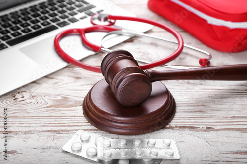 Judge gavel, pills, laptop and stethoscope on wooden background. Concept of health care reform photo