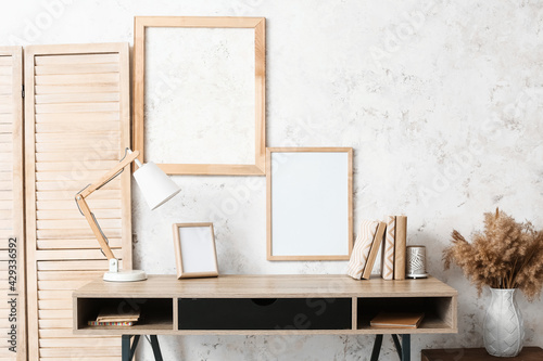 Modern workplace with lamp, frames and books near light wall