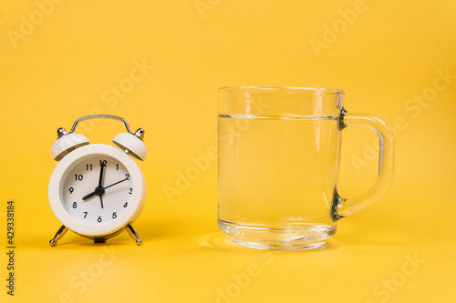 Alarm clock and a glass of water on a yellow background. Wake up early in the morning. Drink water