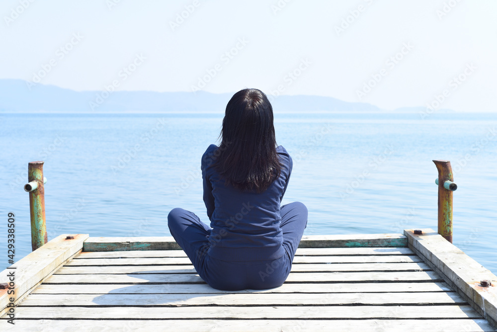 45 y.o. Russian woman sitting in lotus position on a wooden pier against the Japanese sea 