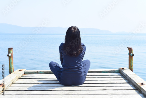 45 y.o. Russian woman sitting in lotus position on a wooden pier against the Japanese sea 